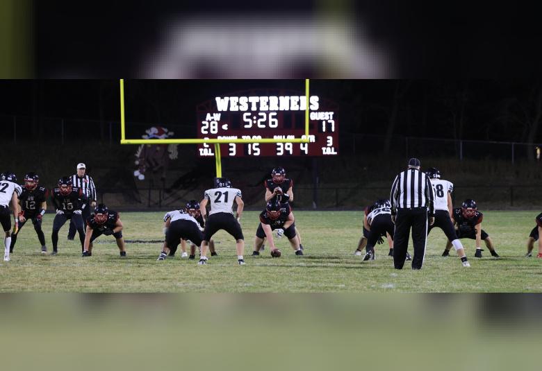 Two referees and a dozen football players are on the field, mid-game. The digital scoreboard reads "A-W 28" and "Guest 17."