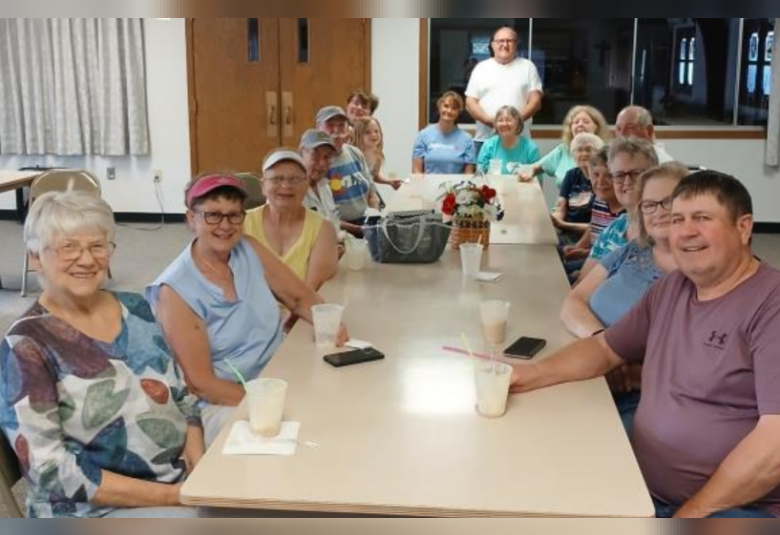 About a dozen people sit on both sides of a long, rectangular table, enjoying their root beer floats.