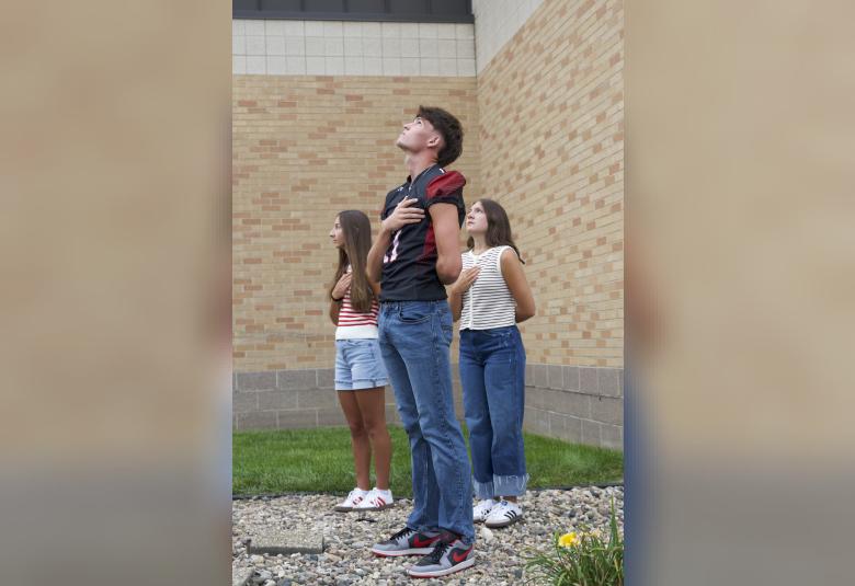 Akron-Westfield seniors Peyton VanderHelm, Reegan McKee, and Callie Jager, who raised the flag, stand with their hands over their hearts as the Star Spangled Banner plays in the background.